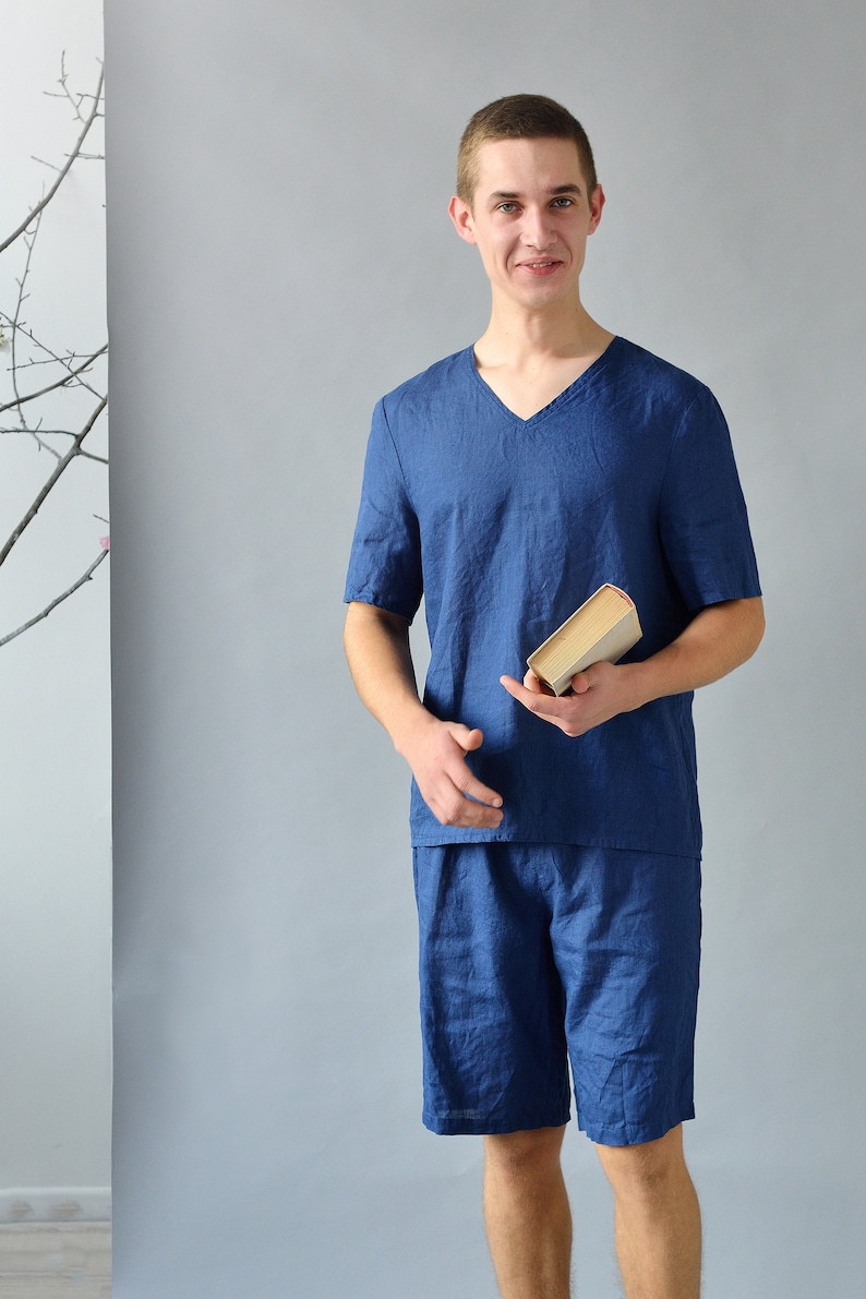 Pode incluir: Um homem vestindo uma camisa de linho azul de manga curta e shorts combinando. Ele est&aacute; segurando um livro na m&atilde;o direita.