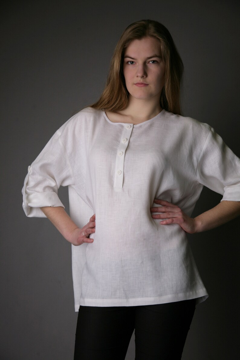 May include: A white linen shirt with a button-up placket and rolled-up sleeves. The shirt is loose-fitting and has a relaxed silhouette.