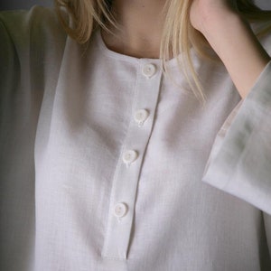 May include: A white linen shirt with a button-up front and long sleeves. The shirt has a relaxed fit and a simple design.