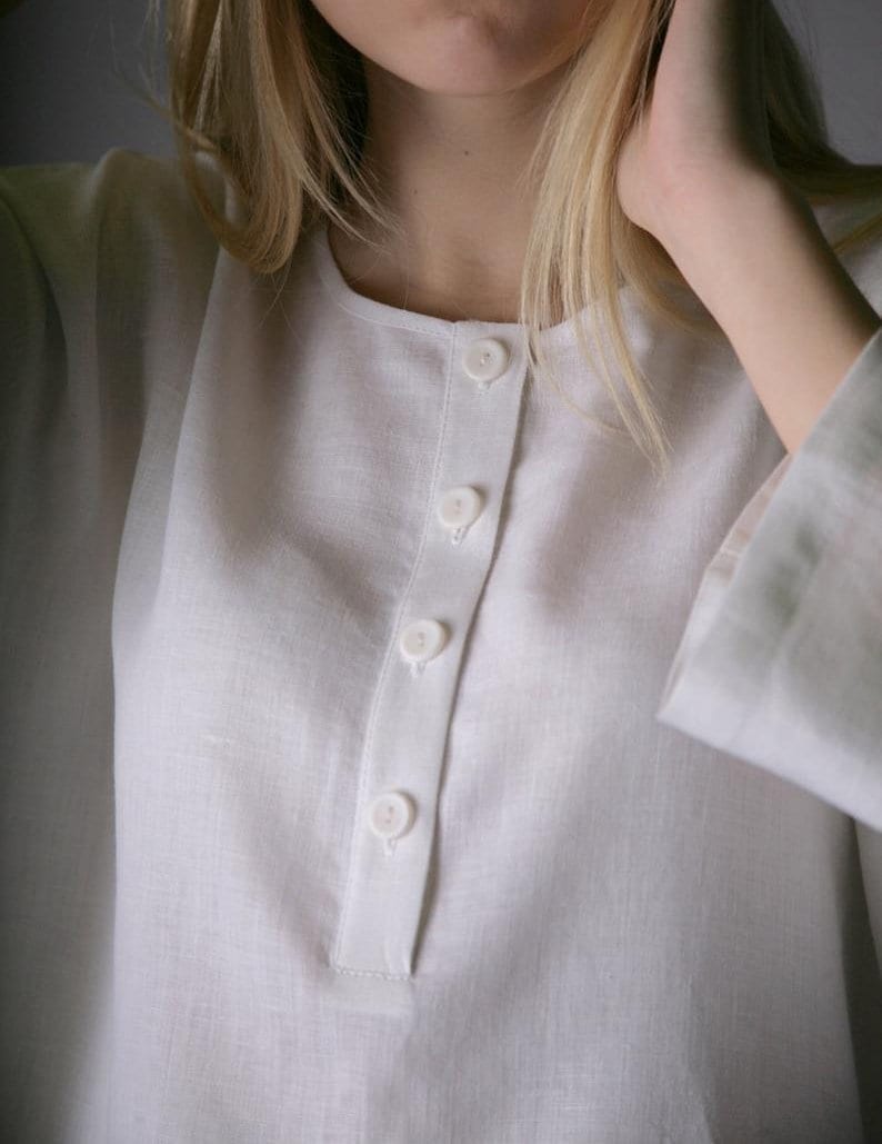 May include: A white linen shirt with a button-up front and long sleeves. The shirt has a relaxed fit and a simple design.