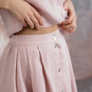 Puede incluir: Una falda de lino rosa claro con cierre de botones y dise&ntilde;o plisado.