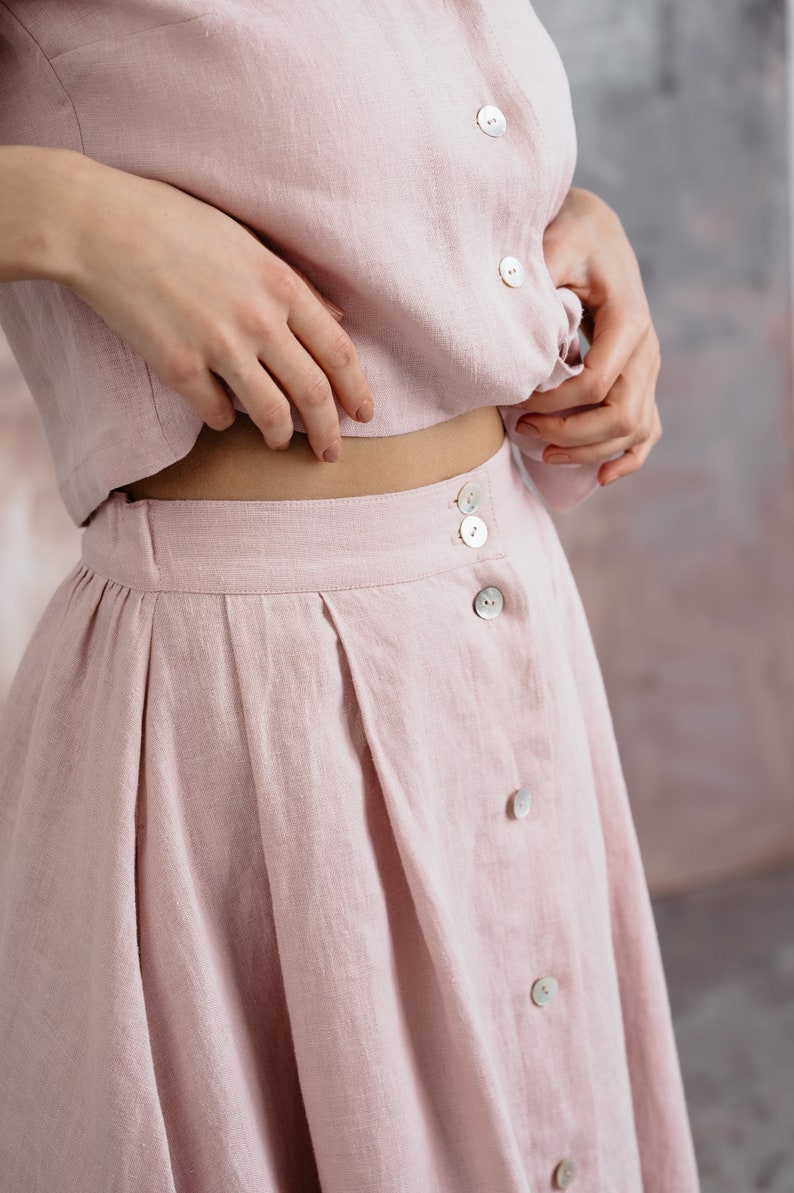 Puede incluir: Una falda de lino rosa claro con cierre de botones y dise&ntilde;o plisado.