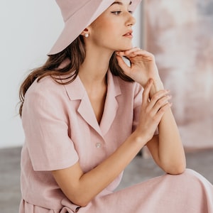 A pink linen short sleeve collared shirt and matching midi skirt. The outfit is accessorized with a wide-brimmed pink hat.