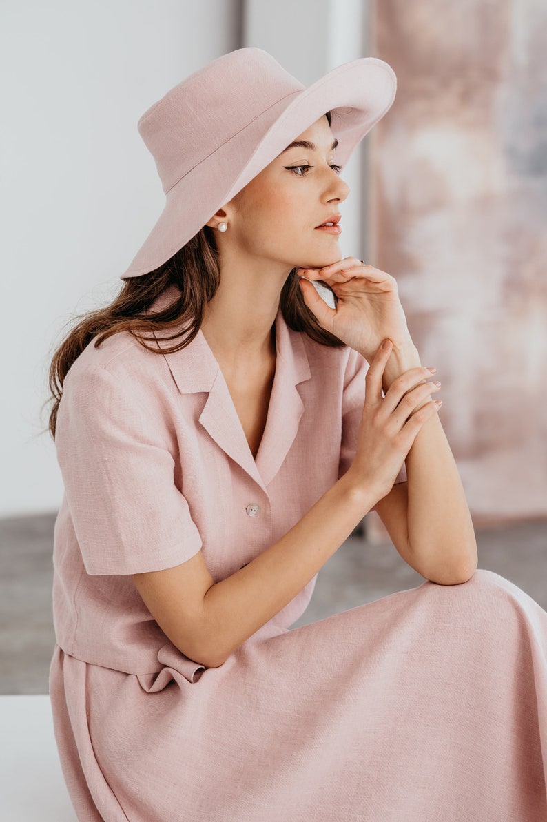 A pink linen short sleeve collared shirt and matching midi skirt. The outfit is accessorized with a wide-brimmed pink hat.