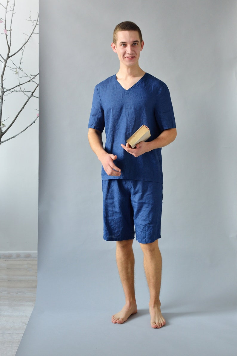 Pode incluir: Um homem vestindo uma camisa de linho azul de manga curta e shorts combinando. Ele est&aacute; segurando um livro em sua m&atilde;o direita.