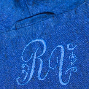 May include: A close-up of a blue fabric with the embroidered initials "R.I." in white thread.