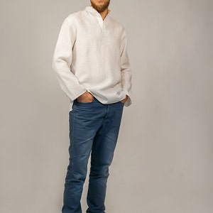 Puede incluir: Un hombre con una camisa de lino blanca con cuello y mangas largas, pantalones vaqueros azules y zapatillas de deporte azul oscuro.