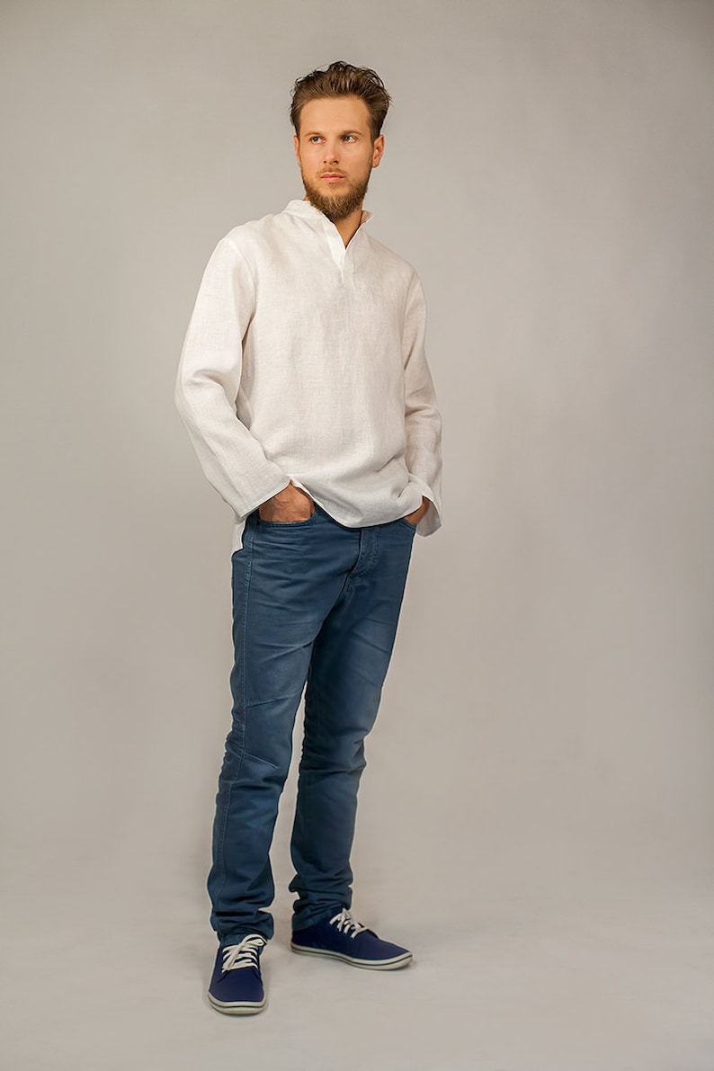 Puede incluir: Un hombre con una camisa de lino blanca con cuello y mangas largas, pantalones vaqueros azules y zapatillas de deporte azul oscuro.