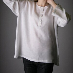 May include: A white linen shirt with a button-up placket and long sleeves. The shirt is loose-fitting and has a relaxed silhouette.