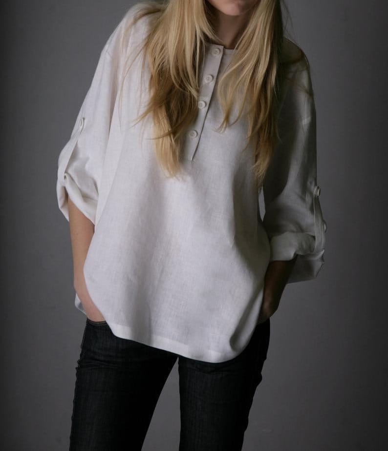 May include: A white linen shirt with a button-up front and rolled-up sleeves. The shirt is loose-fitting and has a relaxed, casual style.