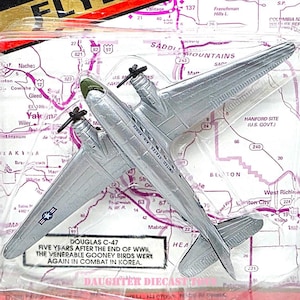 May include: Road Champs diecast metal and plastic Douglas C-47 airplane toy. The silver aircraft has two propellers and is packaged on a map-themed card. The card reads "FLYERS" and "UNITED STATES AIR FORCE".