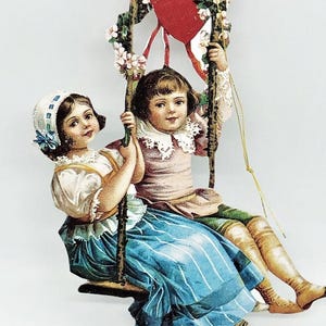 Könnte beinhalten: Eine Vintage-Valentinstagskarte mit zwei Kindern auf einer Schaukel. Die Schaukel ist mit einem roten Herzen und floralen Akzenten verziert. Die Kinder sind in historischer Kleidung gekleidet, das Mädchen in einem blauen Rock und der Junge in einem rosa Hemd.