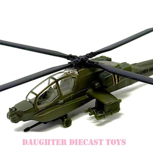 May include: A detailed diecast model of a military helicopter in olive green with black rotor blades. The model features a clear cockpit and intricate detailing, with the text "DAUGHTER DIECAST TOYS" in pink.