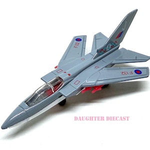 May include: A diecast model airplane in shades of gray, featuring red accents and clear cockpit. The model has the text "F132" and a roundel on the wings and tail. The toy plane is on a white background.