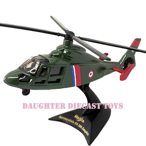 May include: A green diecast model helicopter with black rotors and a stand. The model has red, white, and blue stripes and a roundel. The stand is black and has text that reads "Majisto Aerospatiale SA 365 Dauphin".