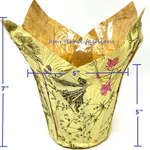 May include: A floral-patterned paper tulip cup with dimensions of 7 inches high, 5 inches wide, and 3.25 inches across the base. The cup features a light yellow background with botanical illustrations and the text "kms floral fashions".
