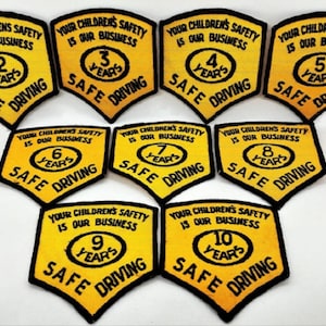 Könnte beinhalten: Eine Sammlung gelb-schwarzer Aufnäher mit dem Text "YOUR CHILDREN'S SAFETY IS OUR BUSINESS" und "SAFE DRIVING". Jeder Aufnäher zeigt eine Zahl von 2 bis 10 Jahren.