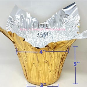 May include: A gold foil container with a silver foil top. The container is 7 inches tall, 4 inches wide at the top, 3 inches wide at the base, and 5 inches deep. The foil has a crinkled texture.