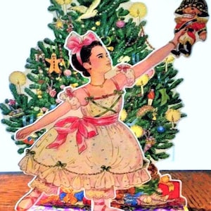 Könnte beinhalten: Vintage Weihnachtskarte mit einer Ballerina, die einen Nussknacker vor einem geschmückten Weihnachtsbaum hält. Die Ballerina trägt eine rosa Schleife, ein Kleid und Schuhe. Die Karte trägt die Aufschrift "Merry Christmas" am unteren Rand.