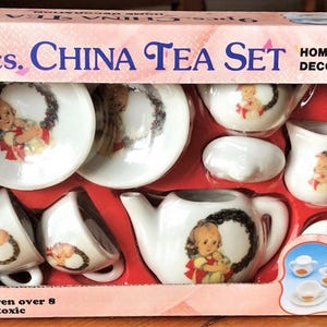 May include: A 9-piece China tea set for children, featuring a teapot, cups, saucers, creamer, and sugar bowl. Each piece is white with a decorative image of a child and a wreath. The box reads "Home Decoration."