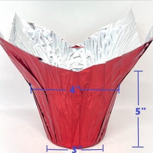 May include: A red foil baking cup with a silver interior. The cup is 7 inches tall, 4 inches wide, and 3 inches across the base. The sides are 5 inches high. The foil is crinkled, giving it a textured appearance.