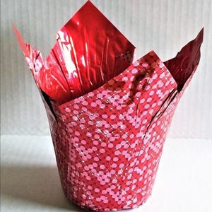 Puede incluir: Una cápsula para hornear en forma de tulipán de papel de aluminio rojo con un estampado de lunares rosas. El interior es de papel de aluminio rojo liso. La cápsula está abierta en la parte superior, revelando el interior rojo.