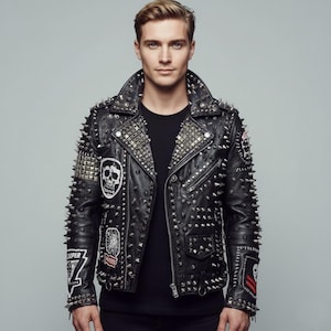 Op de afbeelding: Zwarte leren jas met zilveren studs en spikes. De jas heeft meerdere patches, waaronder een schedelontwerp. De kraag en schouders zijn zwaar bezaaid met studs, wat een gedurfde, edgy look creëert. Een klassieke bikerjack-stijl.