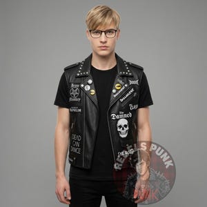 Op de afbeelding: Zwarte leren vest met zilveren studs en patches. Patches bevatten bandnamen als "The Damned" en "Discharge", en de tekst "DEAD CAN DANCE". Het vest wordt gedragen over een zwart t-shirt. Het algemene thema is punkrockmode.