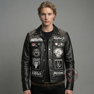 Op de afbeelding: Zwarte leren jas met zilveren metalen spikes op de schouders. De jas heeft meerdere patches met witte tekst en afbeeldingen. Een rij kogelvormige studs is zichtbaar bij de taille. De jas wordt over een zwart shirt gedragen.