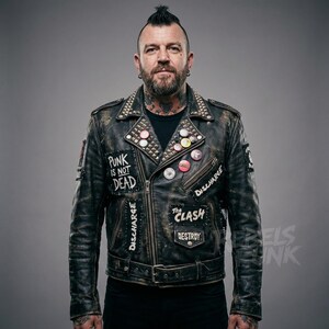 May include: A distressed black leather jacket with metal studs on the collar and shoulders. Patches with the text "PUNK IS NOT DEAD", "DISCHARGE", and "THE CLASH DESTROY" are visible. Several colorful pin-back buttons are also attached.