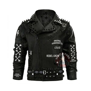 Può includere: Giacca in pelle nera con colletto e spalle borchiate. Presenta toppe con testo tra cui "ORIGINAL HANDCRAFTED LTD ED" e "REBEL CREW". Include grafiche di chiavi e fulmini.