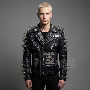 Pode incluir: Casaco de couro preto com pontas prateadas nos ombros e gola. O casaco apresenta patches com caveiras e logotipos de bandas, e o texto "ROCK 'N' ROLL IS DEAD - LONG LIVE ROCK 'N' ROLL".