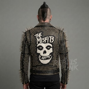 Puede incluir: Chaqueta de cuero negro cubierta de tachuelas y púas plateadas. La espalda presenta un parche blanco con "THE MISFITS" y un gráfico de calavera. La chaqueta tiene un estilo motero clásico con cierre de cremallera y cuello con solapas.