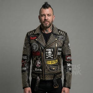 Pode incluir: Jaqueta de couro preta com tachas e patches prateados. Os patches incluem "CLASH", "PUNK'S NOT", "MISFITS" e "SEX PISTOLS". A jaqueta tem zíper, cinto e corrente. Estilo punk rock.