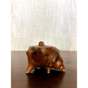 May include: A small, brown, shell-shaped ceramic teapot with a smooth, glossy finish. The teapot features a coiled, spiral design resembling a conch shell, a small spout, and a circular lid with a tiny, raised knob handle at the very top center.
