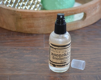 May include: A clear glass bottle with a black spray top and a brown label that reads "Twisted Organics Moonshine Deodorant Key Lime Pepper".
