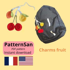 Op de afbeelding: Een zwarte rugzak met een witte streep en een gehaakte fruitbedel. De bedel heeft rode kersen, een oranje vrucht en een gele vrucht. De afbeelding bevat ook de tekst "PatternSan PDF pattern Instant download" en "Charms fruit".