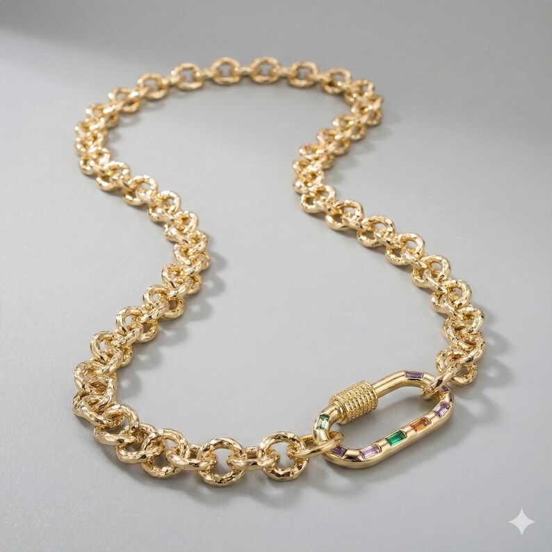 May include: Gold-toned necklace with a textured chain design. The necklace features a decorative clasp with colorful rectangular gemstones. The chain is made of interlocking circular links.
