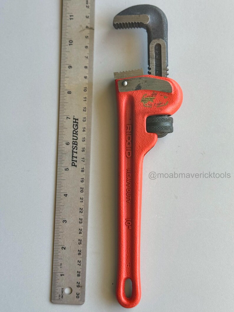 May include: A red and black Ridgid 10-inch pipe wrench with a ruler for scale. The wrench is labeled "HEAVY DUTY" and has a jaw opening. The ruler is marked in inches.