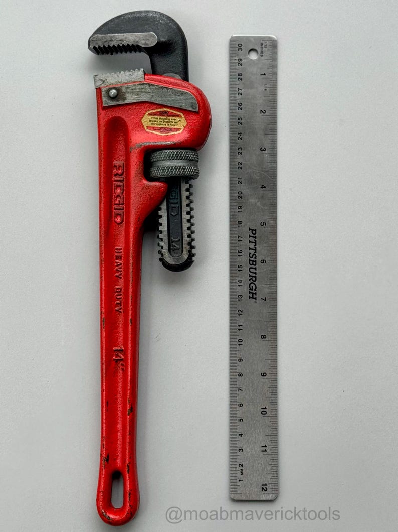 May include: A red Ridgid 14-inch heavy-duty pipe wrench with a black jaw, next to a ruler marked in inches. The wrench has a textured handle and a label. The ruler is marked with the Pittsburgh brand.