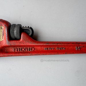 May include: A red Ridgid heavy-duty pipe wrench, 14 inches long. The wrench has a textured handle and adjustable jaws. The brand name and size are printed on the tool.