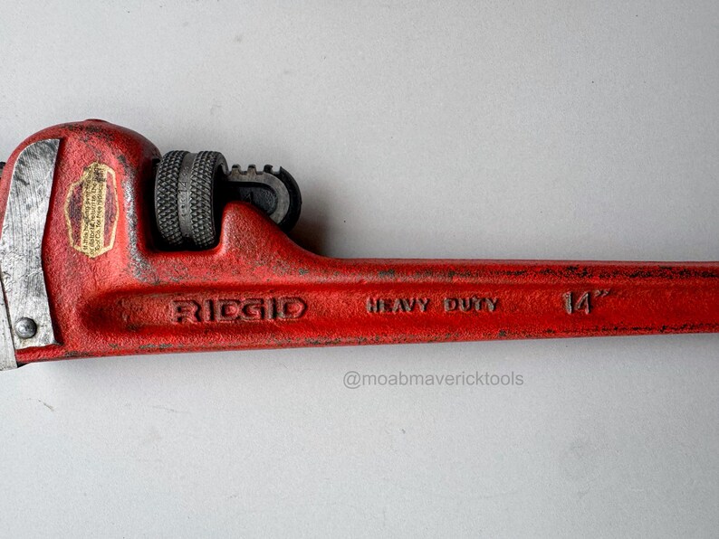 May include: A red Ridgid heavy-duty pipe wrench, 14 inches long. The wrench has a textured handle and adjustable jaws. The brand name and size are printed on the tool.
