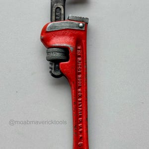 May include: A vintage red pipe wrench with a black head and jaws. The wrench has a textured handle and the text "THE RIDGE TOOL CO. ELYRIA, O. U.S.A." is visible on the handle. The wrench is a tool.