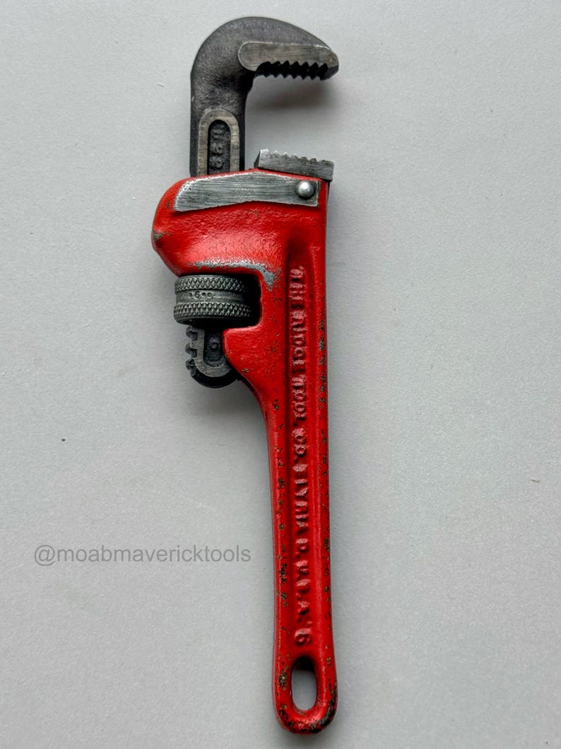 May include: A vintage red pipe wrench with a black head and jaws. The wrench has a textured handle and the text "THE RIDGE TOOL CO. ELYRIA, O. U.S.A." is visible on the handle. The wrench is a tool.