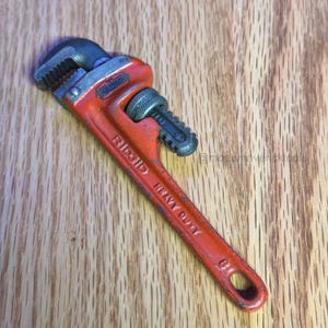 May include: A heavy-duty, orange Ridgid pipe wrench with a black adjustable jaw and handle. The wrench is designed for gripping and turning pipes and other cylindrical objects. The text "Ridgid Heavy Duty" is visible on the handle.