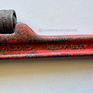 May include: Close-up of a red Ridgid pipe wrench. The wrench is marked "HEAVY DUTY 10" and shows signs of wear. The adjustable jaw is visible, along with the textured adjustment wheel. The tool is designed for plumbing and pipe fitting.