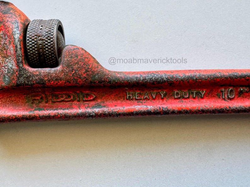 May include: Close-up of a red Ridgid pipe wrench. The wrench is marked "HEAVY DUTY 10" and shows signs of wear. The adjustable jaw is visible, along with the textured adjustment wheel. The tool is designed for plumbing and pipe fitting.