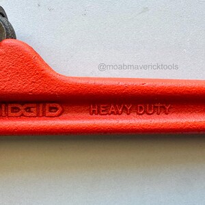 May include: A close-up of a red RIDGID heavy-duty pipe cutter. The tool is 10 inches long and features a black textured grip. The text "RIDGID", "HEAVY DUTY", and "10" are visible on the tool.