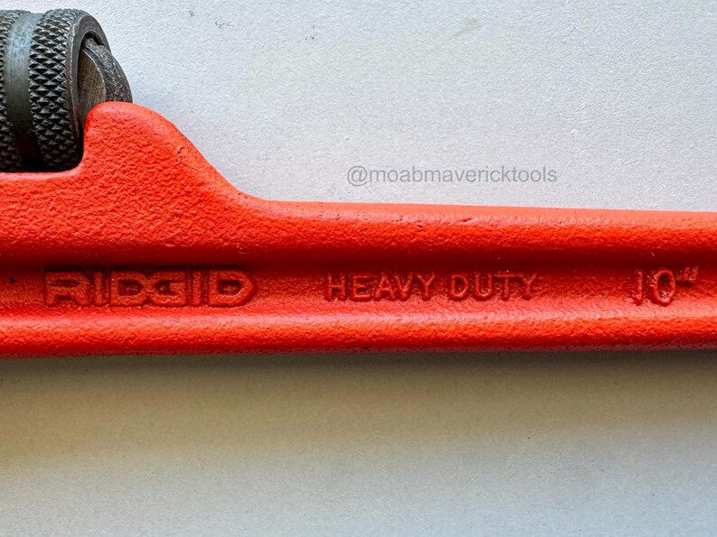May include: A close-up of a red RIDGID heavy-duty pipe cutter. The tool is 10 inches long and features a black textured grip. The text "RIDGID", "HEAVY DUTY", and "10" are visible on the tool.