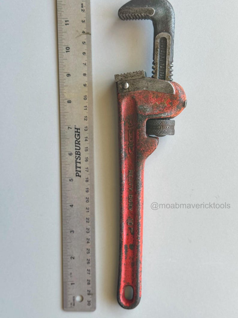 May include: A vintage red and black heavy-duty pipe wrench with a Pittsburgh ruler. The wrench is approximately 10 inches long. The wrench has a textured handle and adjustable jaws. The text "Heavy Duty 10" is visible on the handle. The Instagram handle @moabmavericktools is also visible.